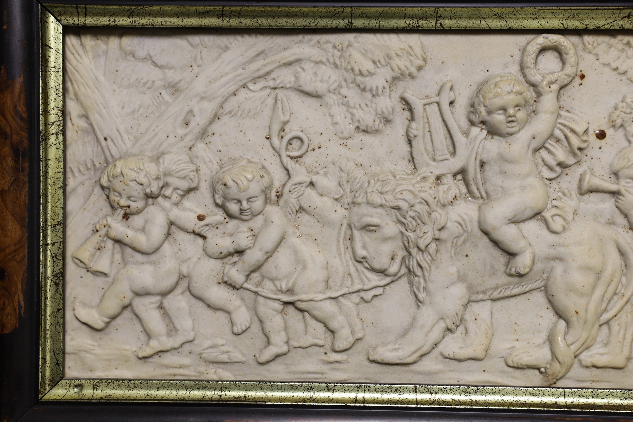 A framed ceramic relief plaque of classical scene with putti 16x31cm excl frame